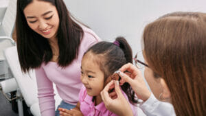 Young girl at the doctor with her mother getting her hearing aid placed.