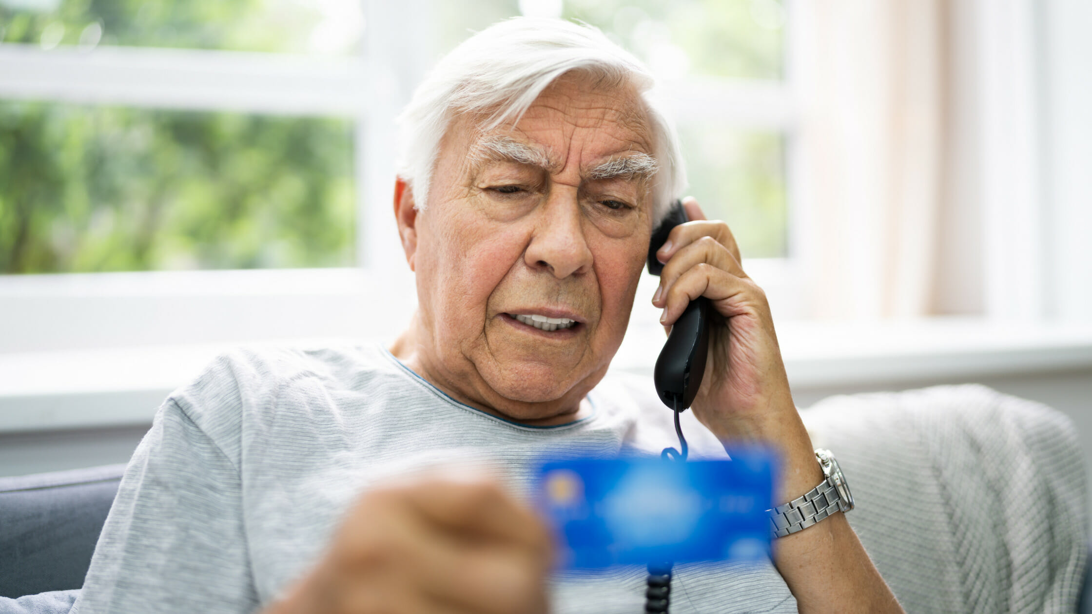 elderly man talking on the phone while holding his credit or debit card.